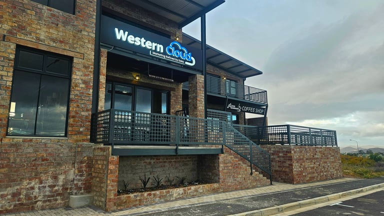 Modern brick building with Western Loops storefront and metal railings, outdoor covered entrance area under cloudy sky